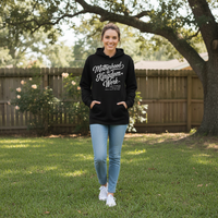 Woman wearing a black hoodie with text, standing outdoors in a backyard.