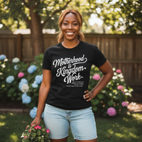 Woman wearing a black t-shirt with text, standing outdoors with flowers and trees in the background